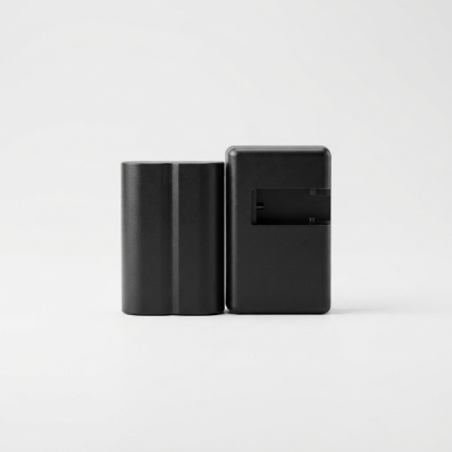 Black camera battery and charger travel kit on matte off-white background