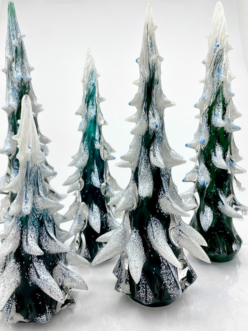 May include: Four glass Christmas tree ornaments in various sizes. The ornaments are green with white glitter and blue accents. The ornaments are arranged on a white surface.