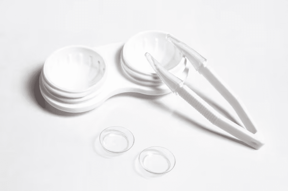 A pair of white contact lens cases with their lids off, and a pair of tweezers on a white background.