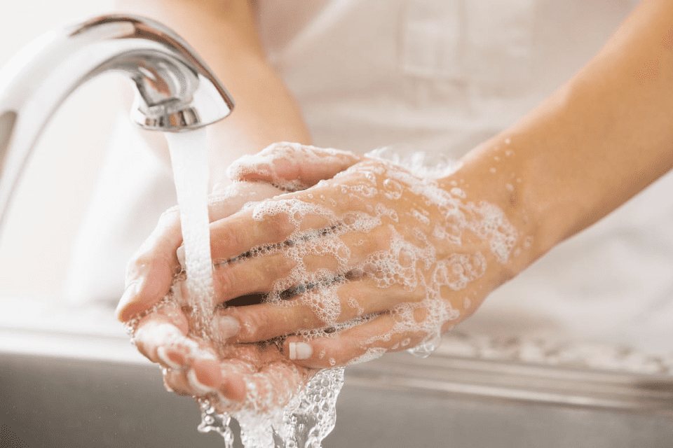 A person washing hands under a running faucet, with soap lather covering hands.