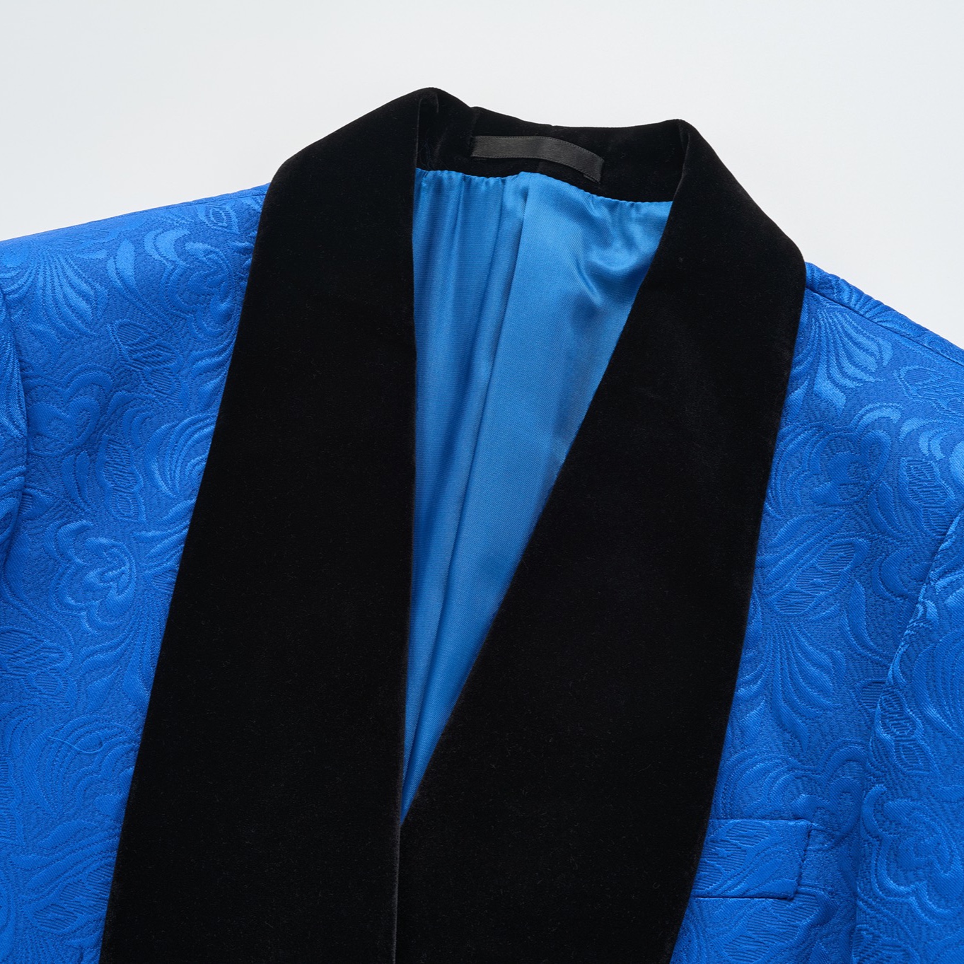 Back view of a vibrant blue jacquard suit jacket with a black velvet shawl collar and intricate floral pattern.