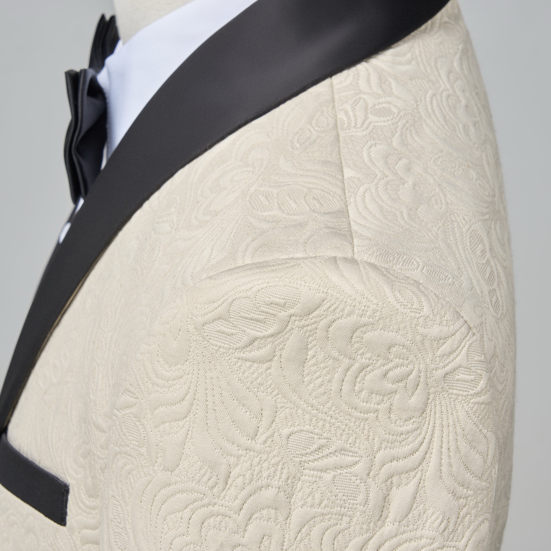 Front view of a men's cream jacquard tuxedo jacket with black satin shawl lapel and one-button closure