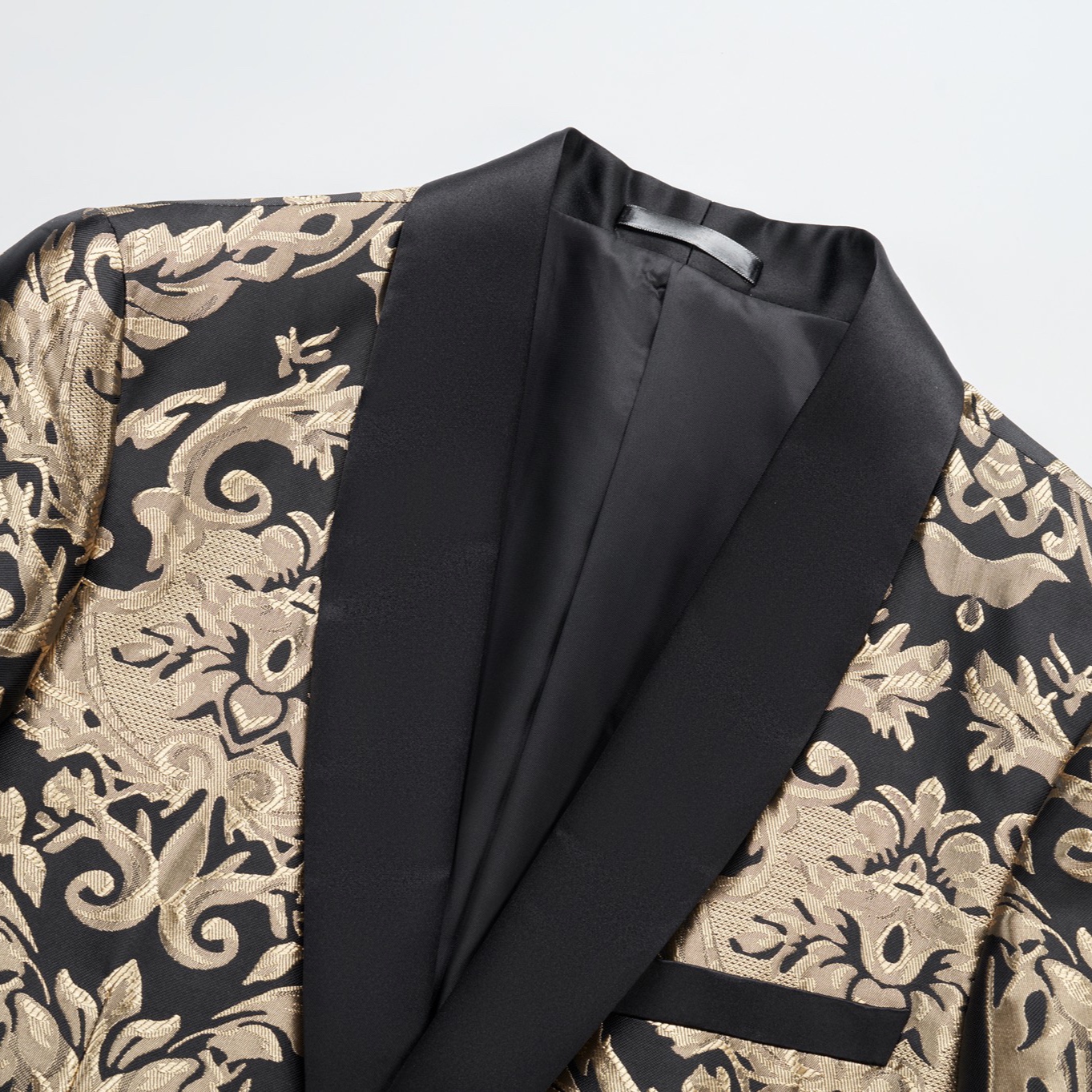 Front view of a men's black and gold damask patterned blazer with a black satin shawl lapel and one button closure.