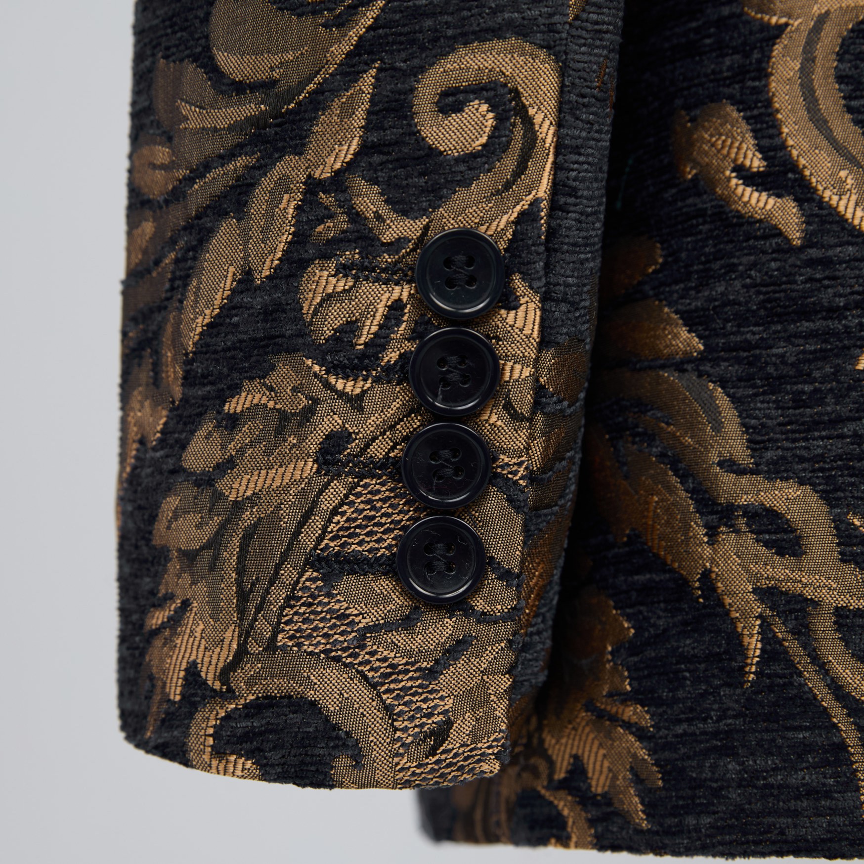 Front view of a men's black and gold damask patterned tuxedo suit with a black satin shawl lapel and one button closure.