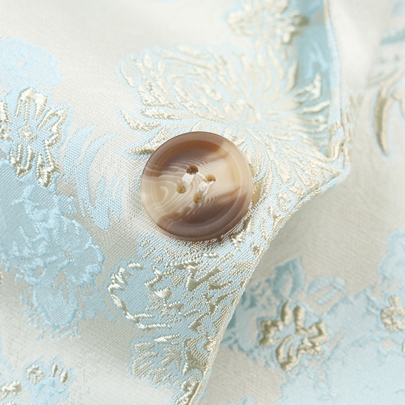 Close-up of a men's light blue and cream floral brocade suit jacket with a single marbled brown button.