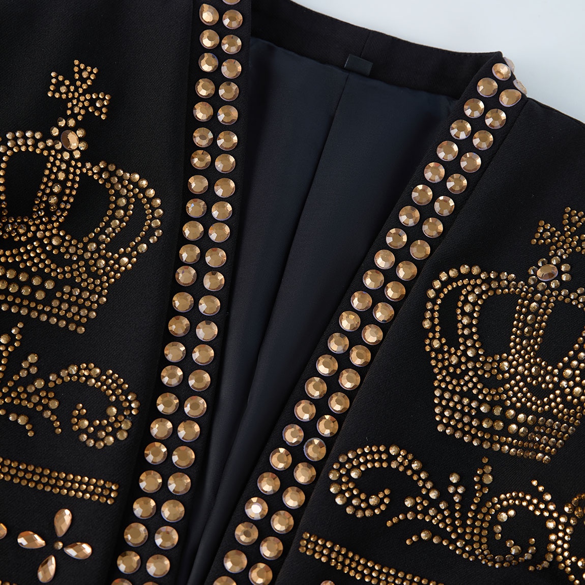Front view of a black men's blazer adorned with gold studs forming crown and scroll patterns.