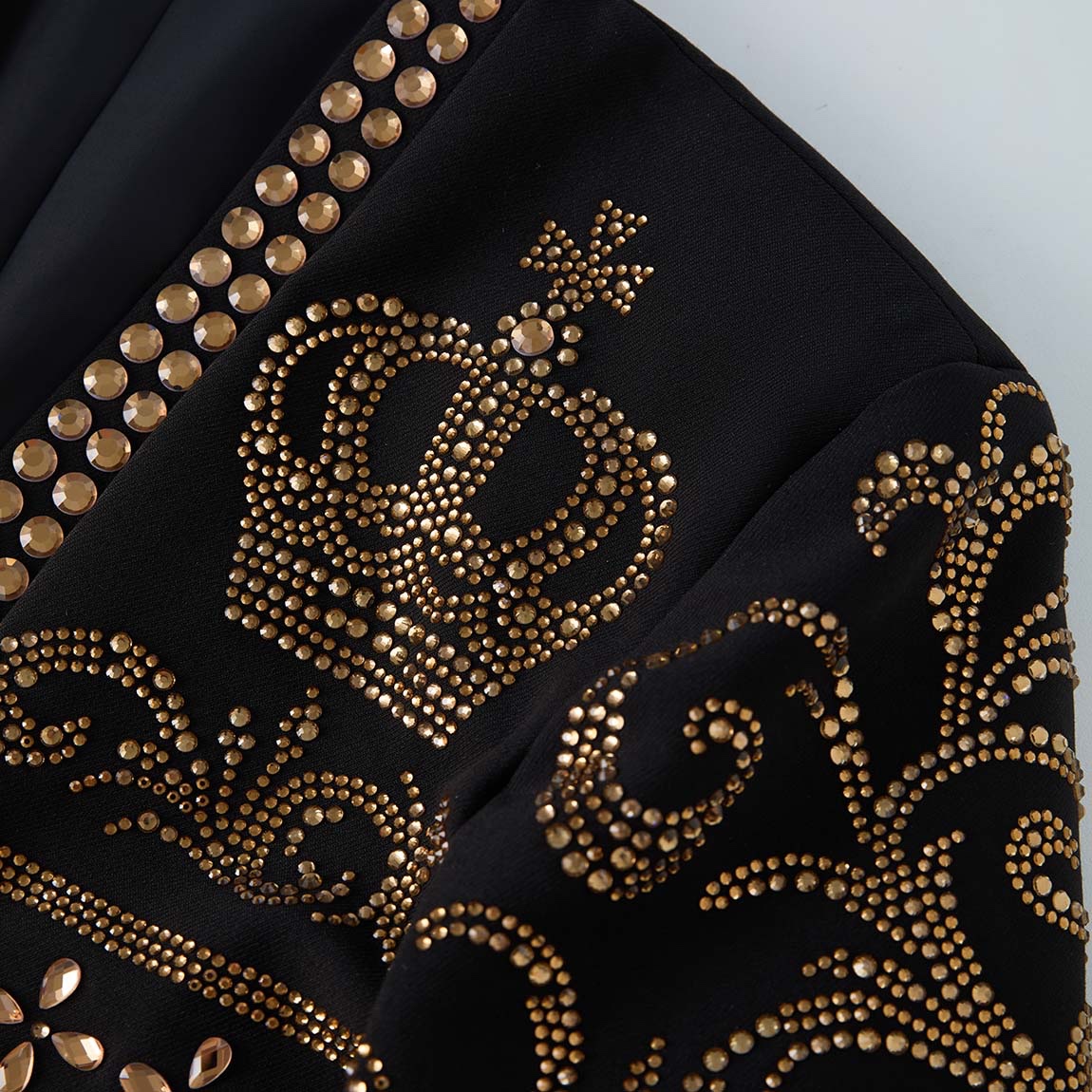 Front view of a black men's blazer adorned with gold studs forming crown and scroll patterns.
