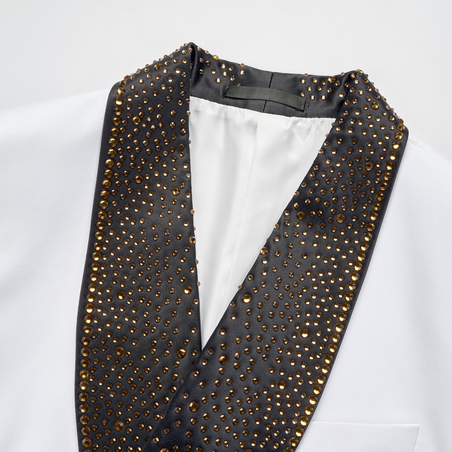 Front view of a men's white tuxedo jacket featuring a black rhinestone-embellished shawl lapel, a unique silver buckle