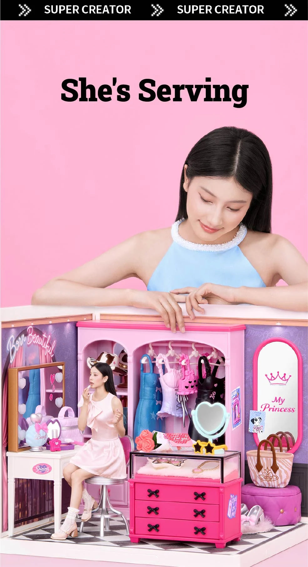 Person leaning over a miniature pink closet room, with a vanity, clothing rack, pink drawers, handbags and checkered floor visible.