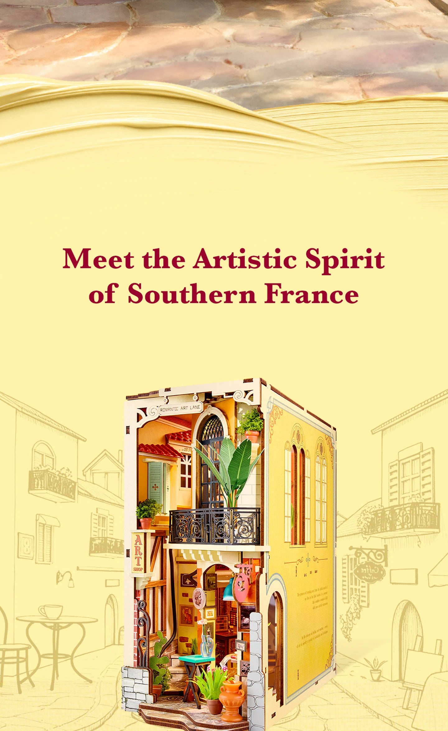 Rolife miniature art shop diorama in yellow and cream, with balcony, plants and shop front, shown against sketched Southern French street buildings.
