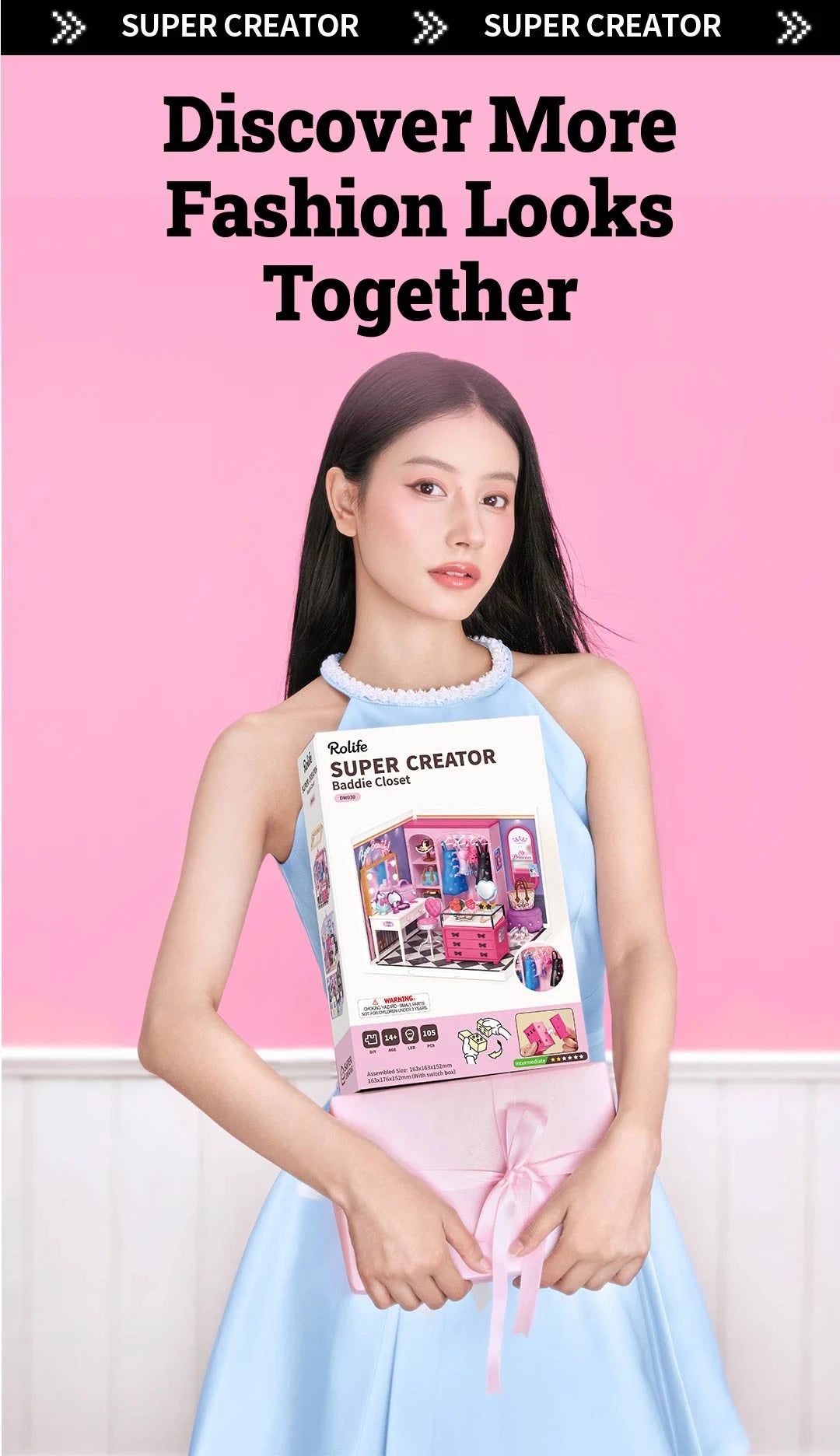Person in a blue dress holding a Rolife Super Creator Baddie Closet box showing the pink miniature dressing room on the front.