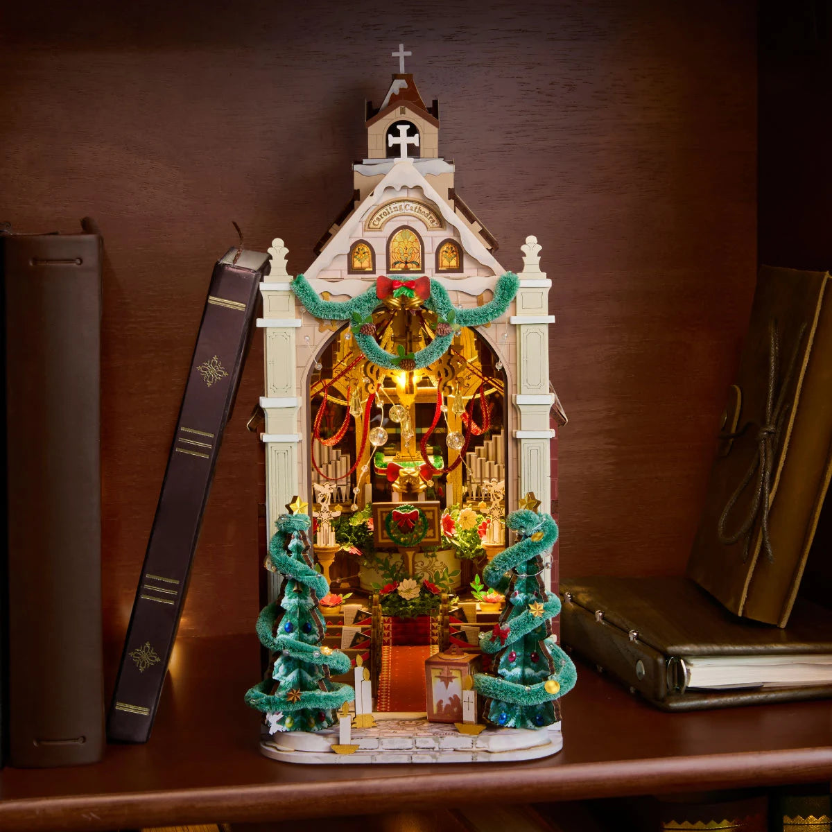 Rolife Caroling Cathedral displayed as a warmly lit book nook between books on a wooden shelf