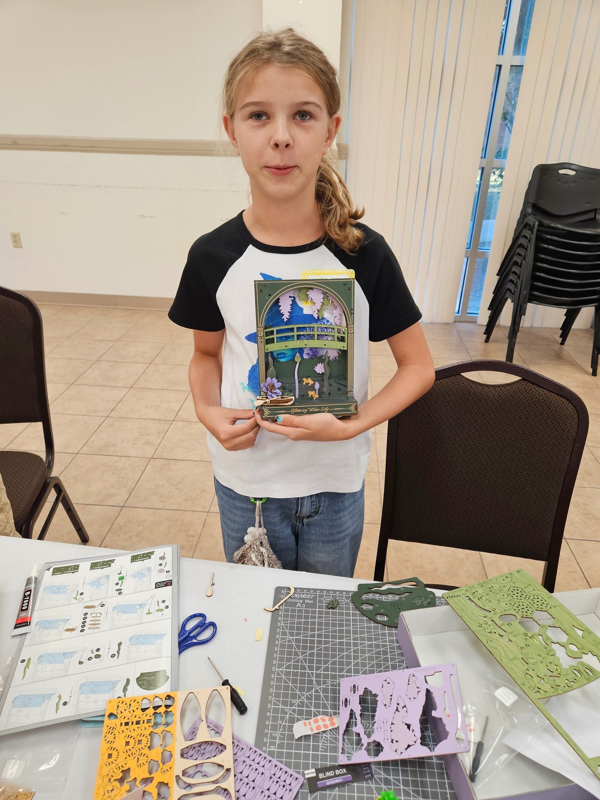 A young builder holding a layered wooden water lily project