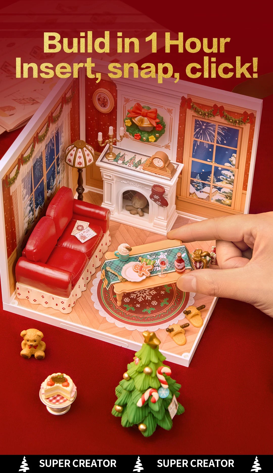 Hand inserting a miniature table into the Christmas Eve room box, with loose teddy bear, cake slice and decorated Christmas tree pieces in front.