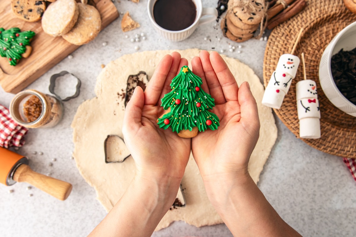 Hands holding a decorated homemade Christmas cookie above a baking table