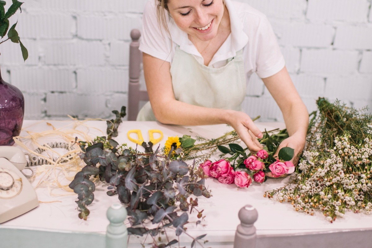 Woman arranging fresh flowers and greenery at a craft table