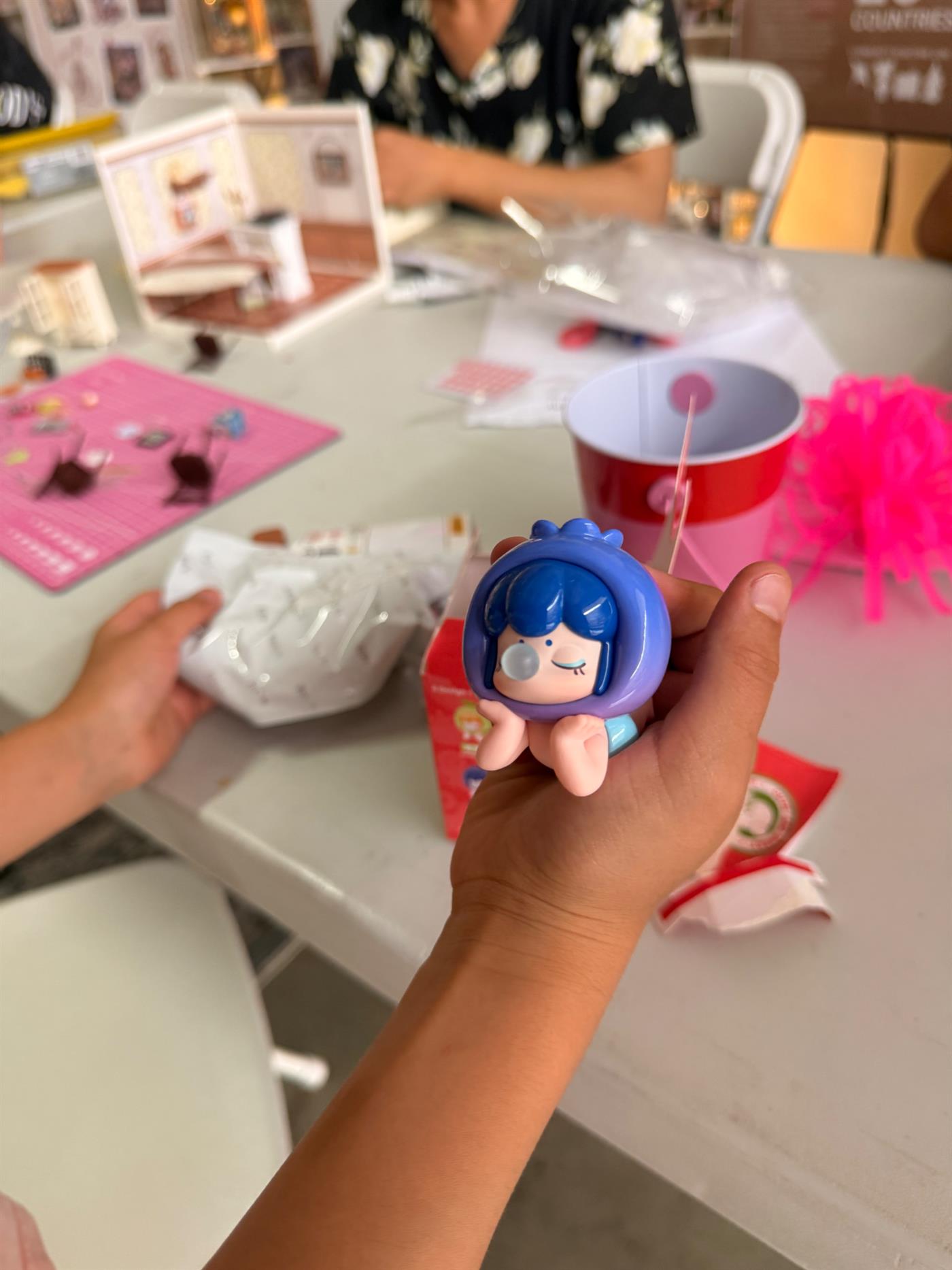 A child shows a tiny blue figure while crafting at a table in Lake Elsinore