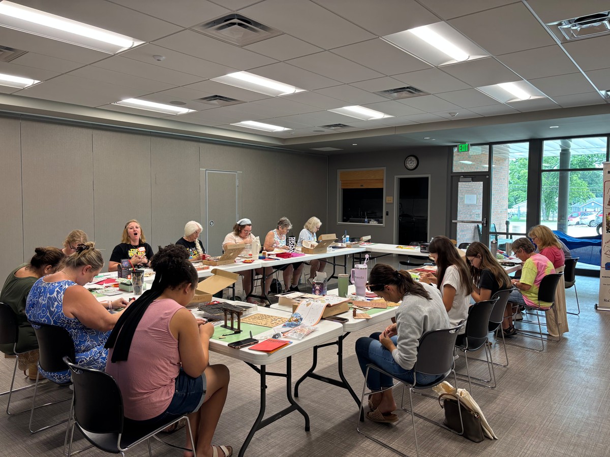 Makers seated face to face around a rectangular table in North Webster