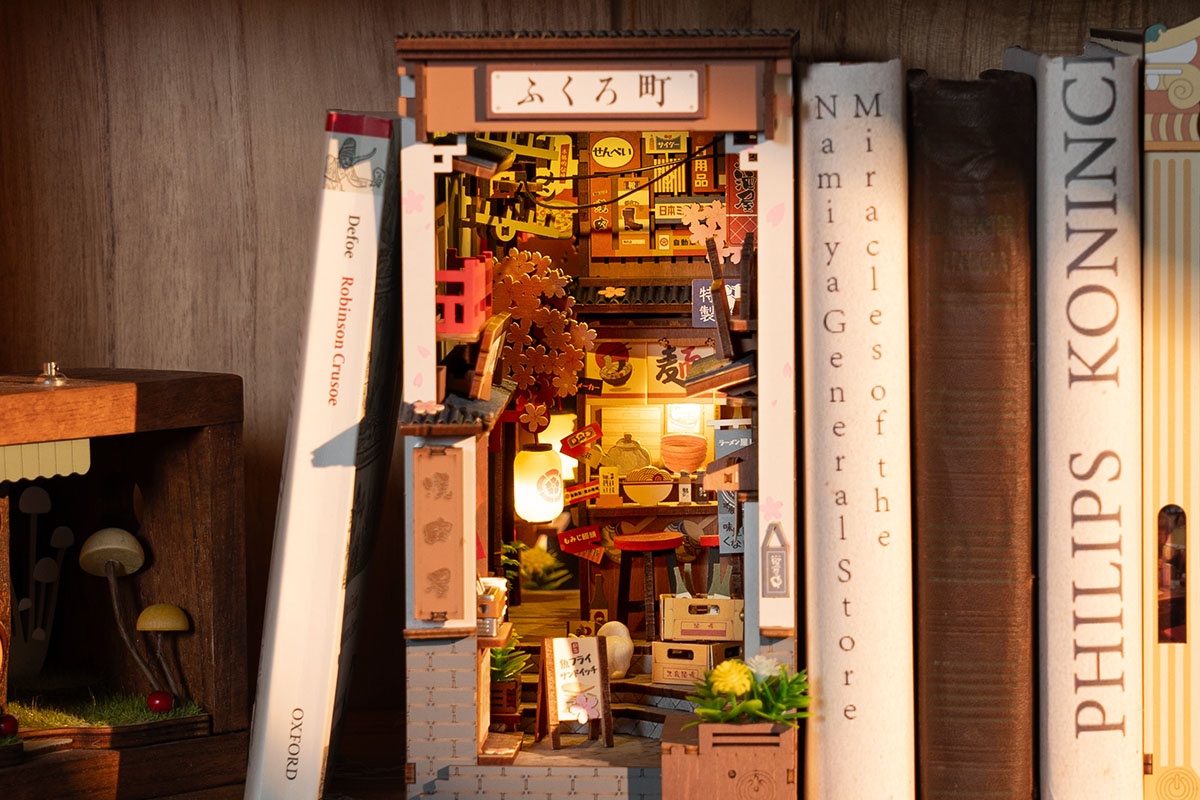 Rolife Sakura Wine Alley book nook glowing between books in a Japanese-inspired reading corner