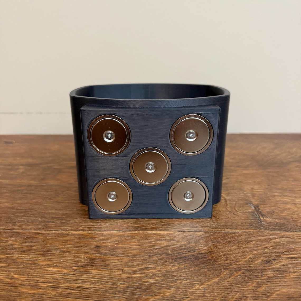 May include: A black plastic container with six silver magnets on the front. The magnets are arranged in a 2x3 grid.