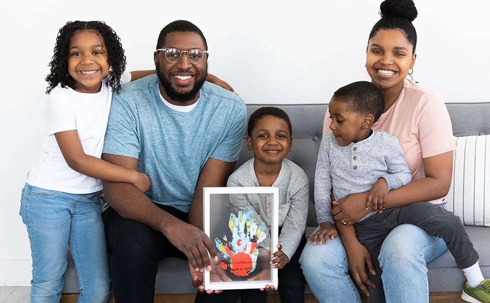 Family sitting on couch together and holding completed handprint frame 