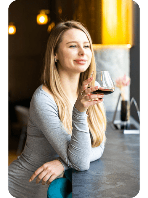 Blonde woman enjoying wine from an Aequilibrium glass by Audacem, highlighting its elegant design