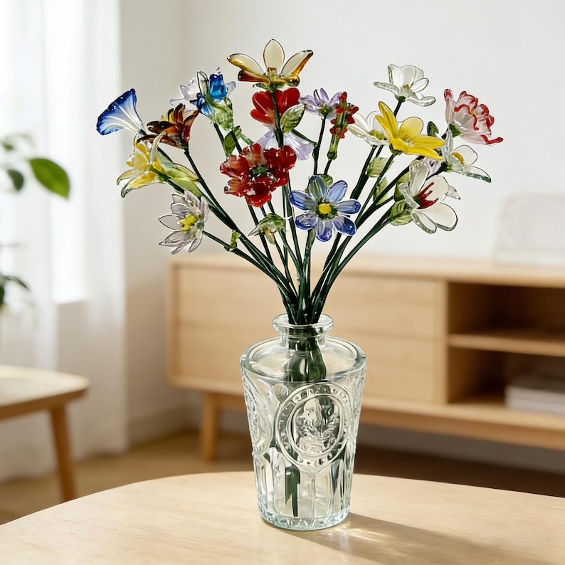 May include: A clear glass vase filled with a vibrant bouquet of glass flowers. The flowers are in various colours, including red, yellow, and blue. The vase has a decorative design and sits on a wooden table.