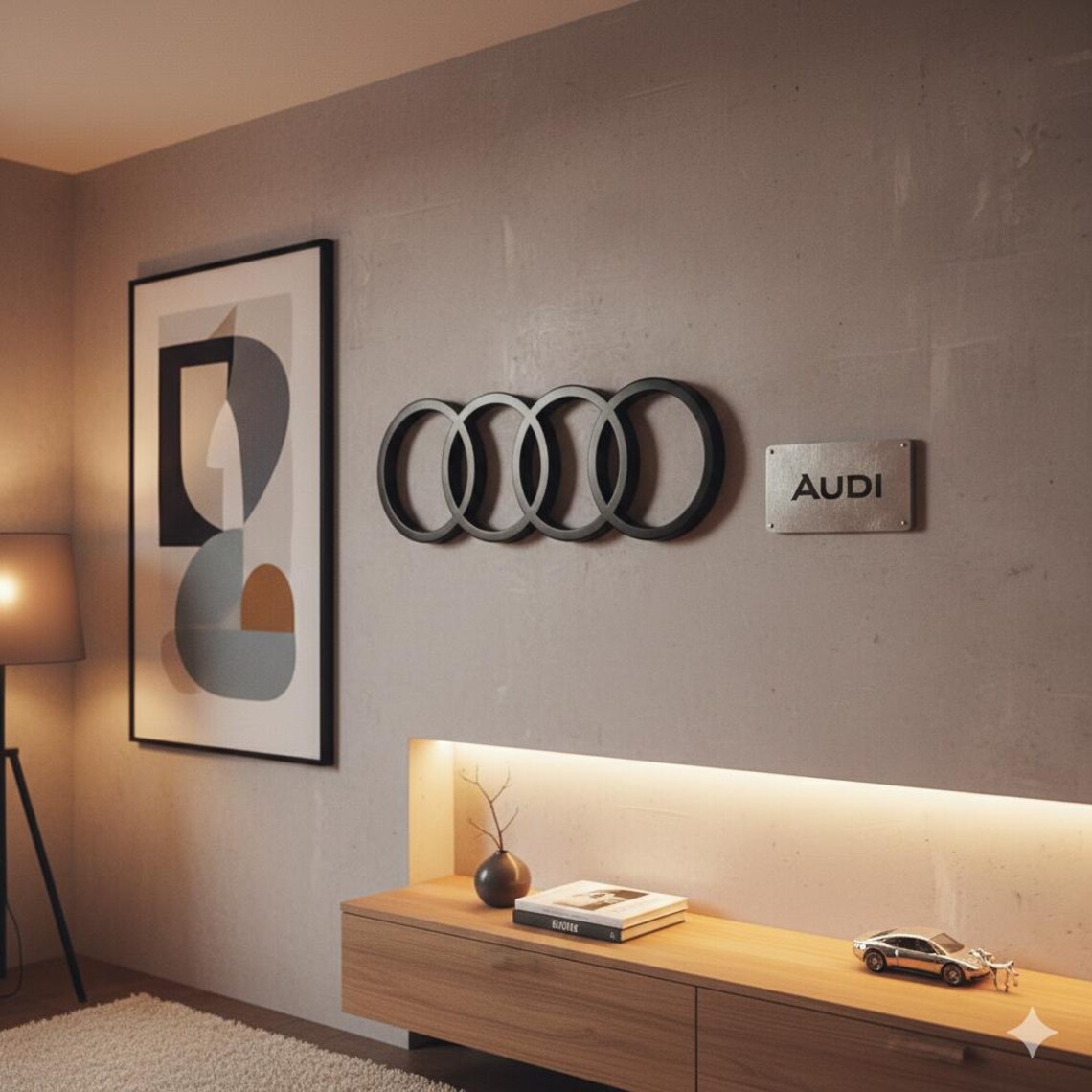 May include: A wall-mounted black Audi logo with four interlocking rings, and a small metal sign that reads "AUDI". The logo is above a wooden cabinet with a lamp and artwork.