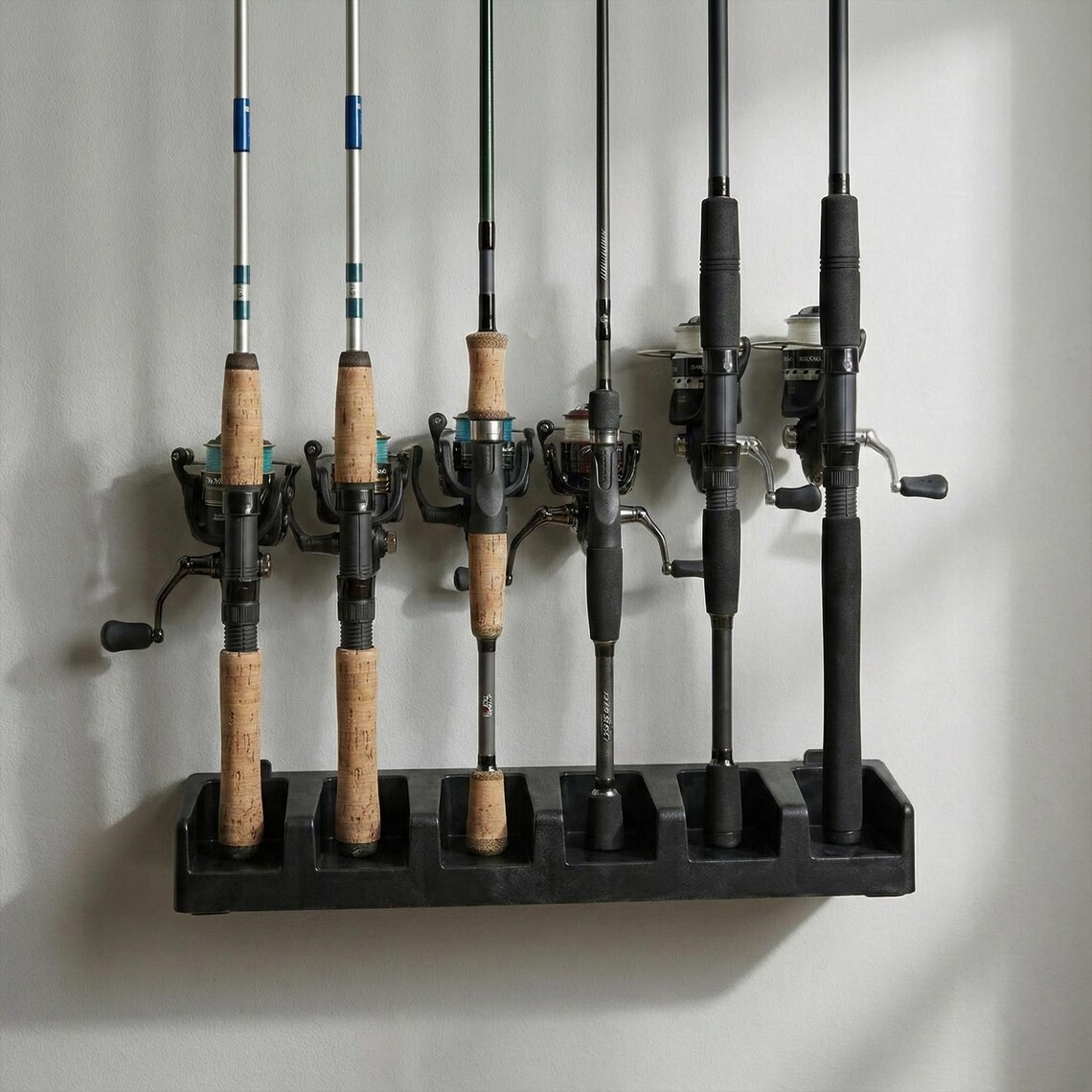 可能包括：一个黑色鱼竿架，上面放着六根鱼竿。这些鱼竿配有黑色和银色的渔线轮、软木手柄，竿身颜色各异。鱼竿架安装在白色墙面上。