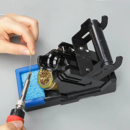 a hand tinning the solder iron beside a soldering iron holder