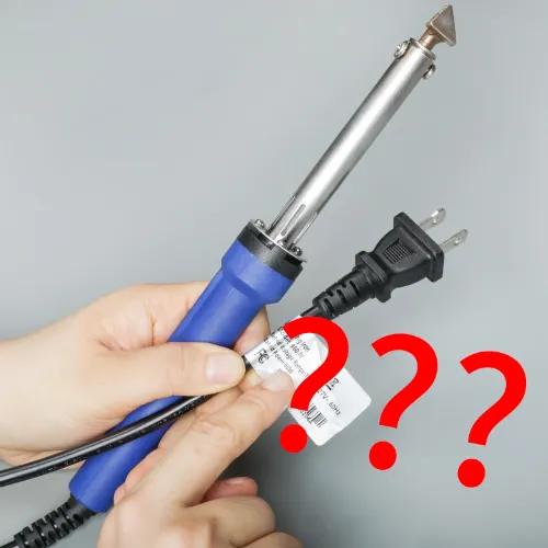 a hand pointing to a soldering iron's power rating label