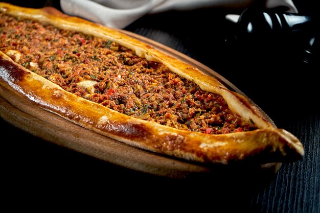 Photo turkish pide with minced lamb, tomatoes, bell pepper served on wooden tray. black table