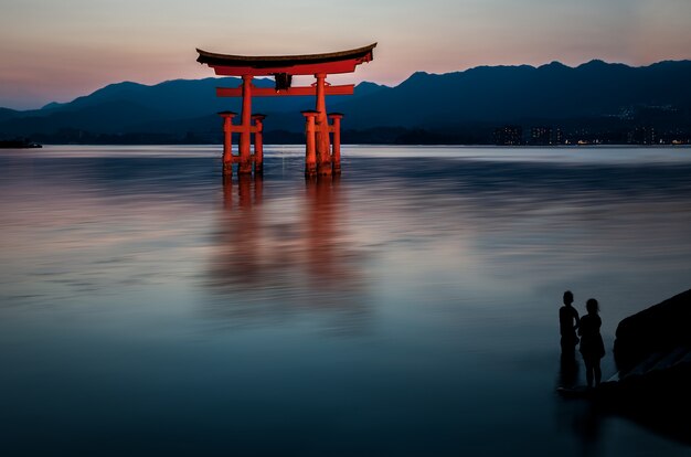 Photo gratuite d'un beau tirage d'une construction rouge dans l'eau avec des silhouettes humaines la regardant.