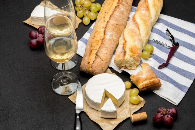 Photo brie cheese, baguette and two glasses of white wine on dark concrete background
