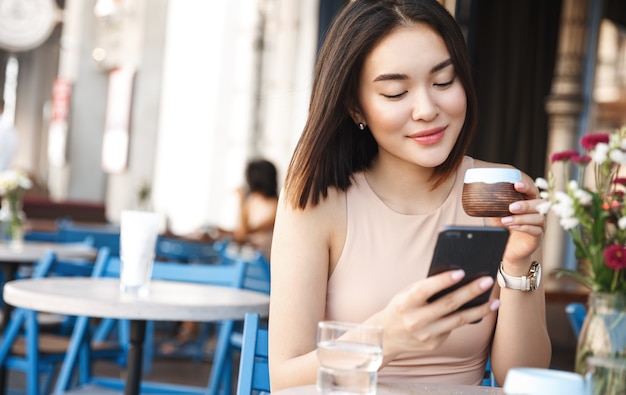 Free photo charming asian woman with beautiful smile reading good news on mobile phone during rest in coffee shop