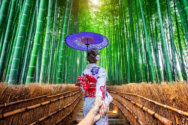 Photo gratuite d'une femme portant un kimono traditionnel japonais tenant la main d'un homme et le conduisant dans une forêt de bambous à Kyoto, Japon.