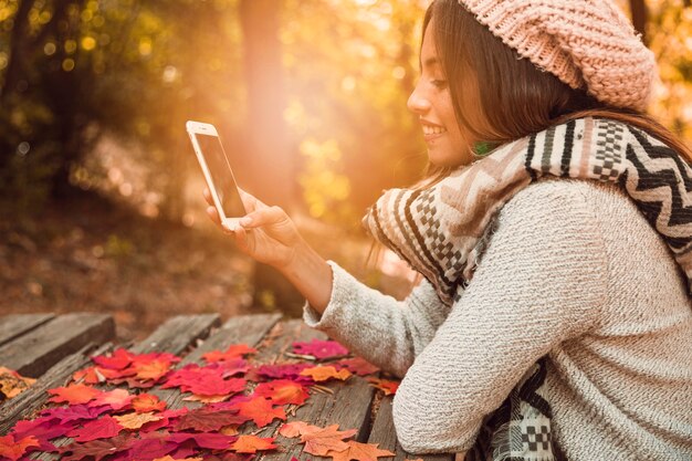 Free photo young female browsing smartphone at table in autumn park