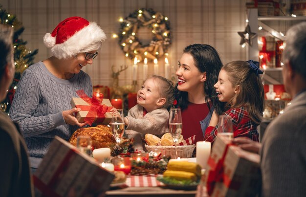 写真 メリークリスマス! 幸せな家族が家で夕食をとっています。 木の近くでの祝祭と団らん。