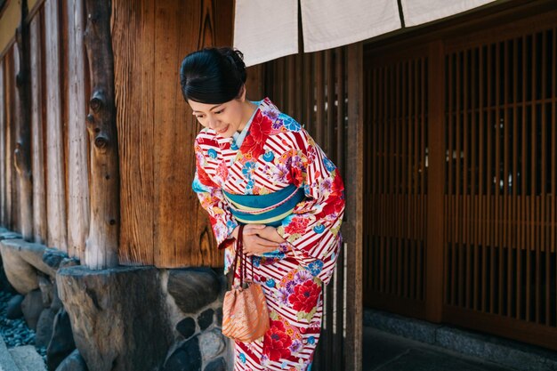 Photo japanese lady bowing in front of her house with beautiful kimono. traditional lifestyle in jp. attractive woman with colorful kimono clothing in summer.