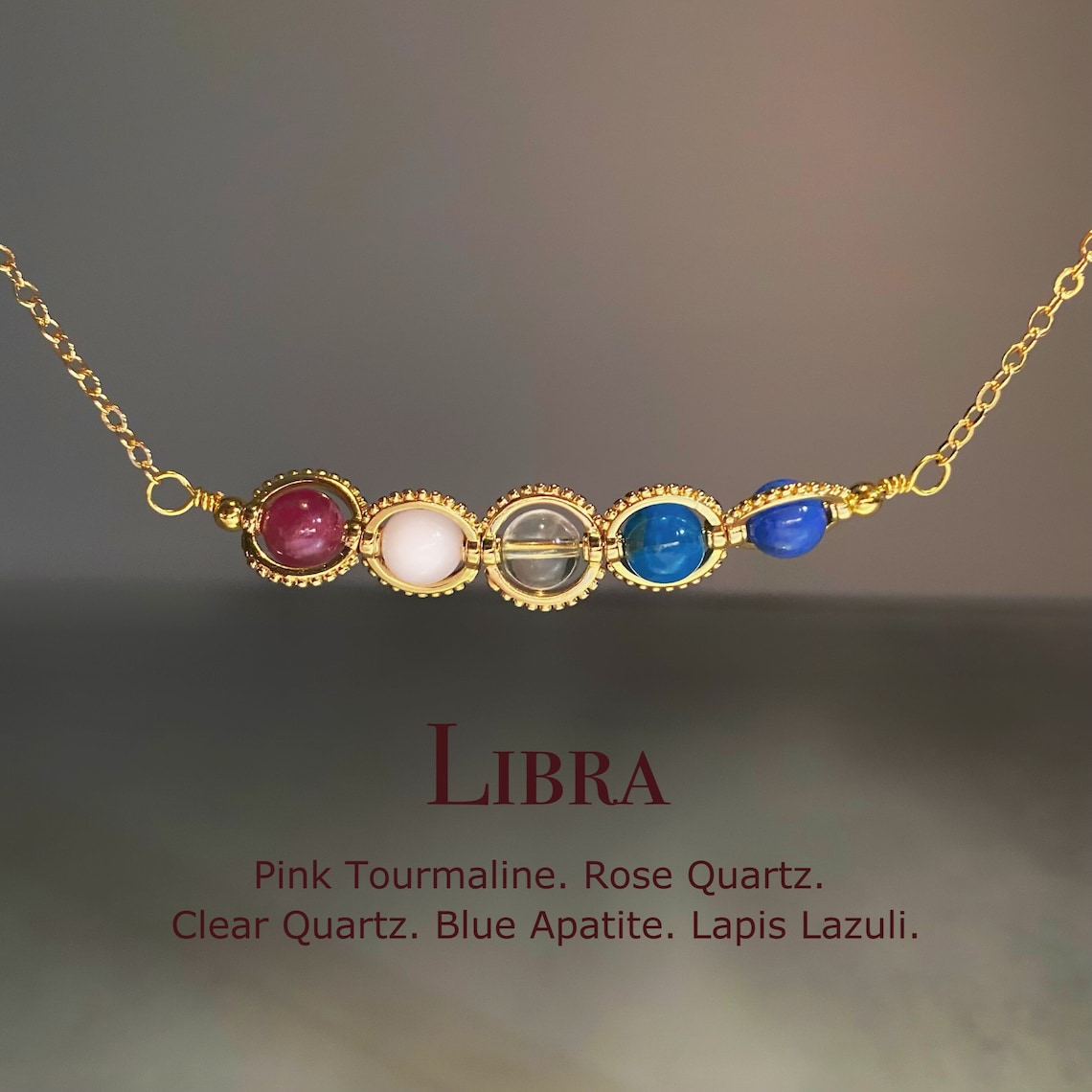 May include: A gold chain necklace with five gemstone beads. The beads are pink tourmaline, rose quartz, clear quartz, blue apatite, and lapis lazuli. The necklace is labeled 'LIBRA' and the stones are listed below. Pink Tourmaline. Rose Quartz. Clear Quartz. Blue Apatite. Lapis Lazuli.