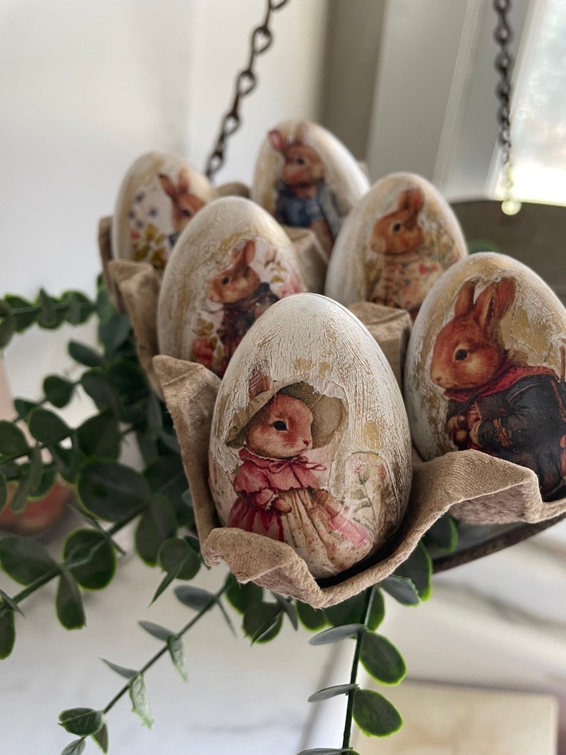 May include: Six white Easter eggs decorated with bunny illustrations. The eggs are in a brown egg carton. The eggs are decorated with different bunny illustrations, including a bunny in a dress, a bunny in a suit, and a bunny with a bow tie.
