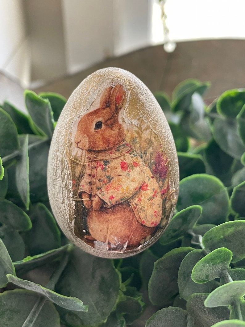 May include: A decorative Easter egg with a beige background and a vintage-style image of a rabbit wearing a floral dress.