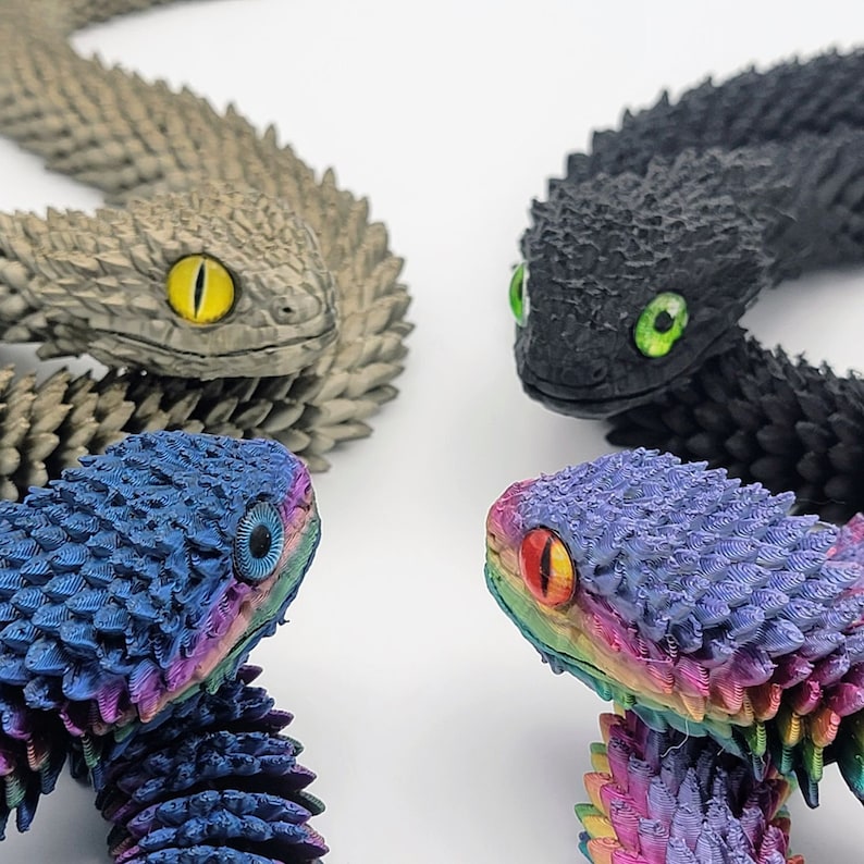 可能包括：三条 3D 打印蛇形雕塑。一条蛇是灰色的，一条是黑色的，有绿色的眼睛，一条是蓝色的，有彩虹色的鳞片。