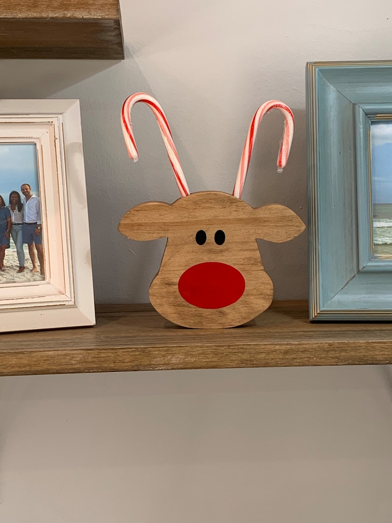 May include: A wooden reindeer head with red painted nose and eyes. Two candy canes are placed in the holes for the antlers.