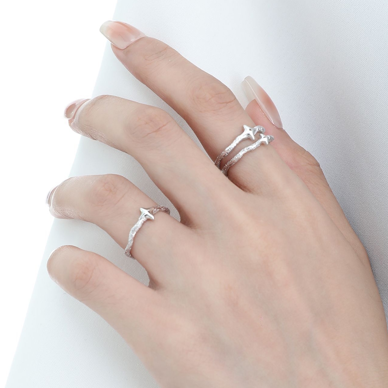 Side view of Starla N°6 and N°7 stackable star rings on finger, 925 sterling silver adjustable band