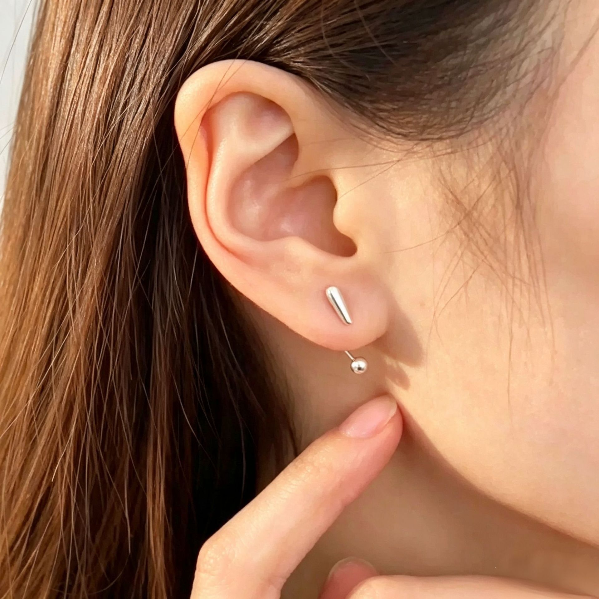 Minimalist silver punctuation earrings shown on ear