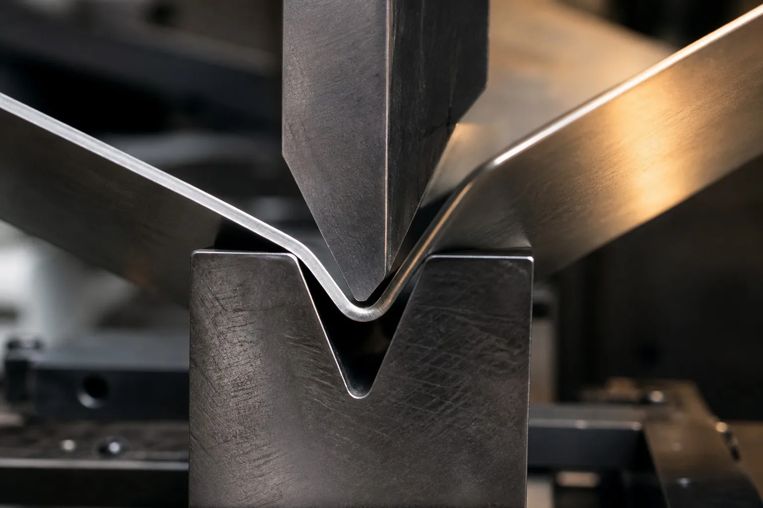 Close-up of a stainless steel sheet being air-bent over a V-shaped lower die on a compact press brake