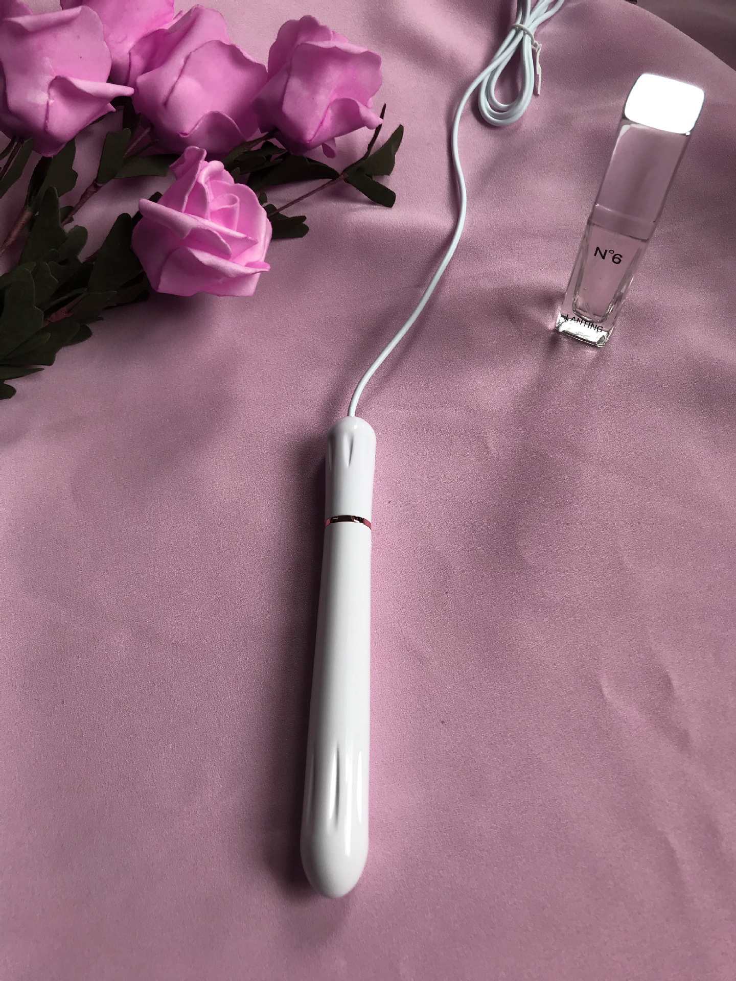 Lilysuck USB Heating Rod on pink fabric with artificial pink roses and No. 6 perfume bottle