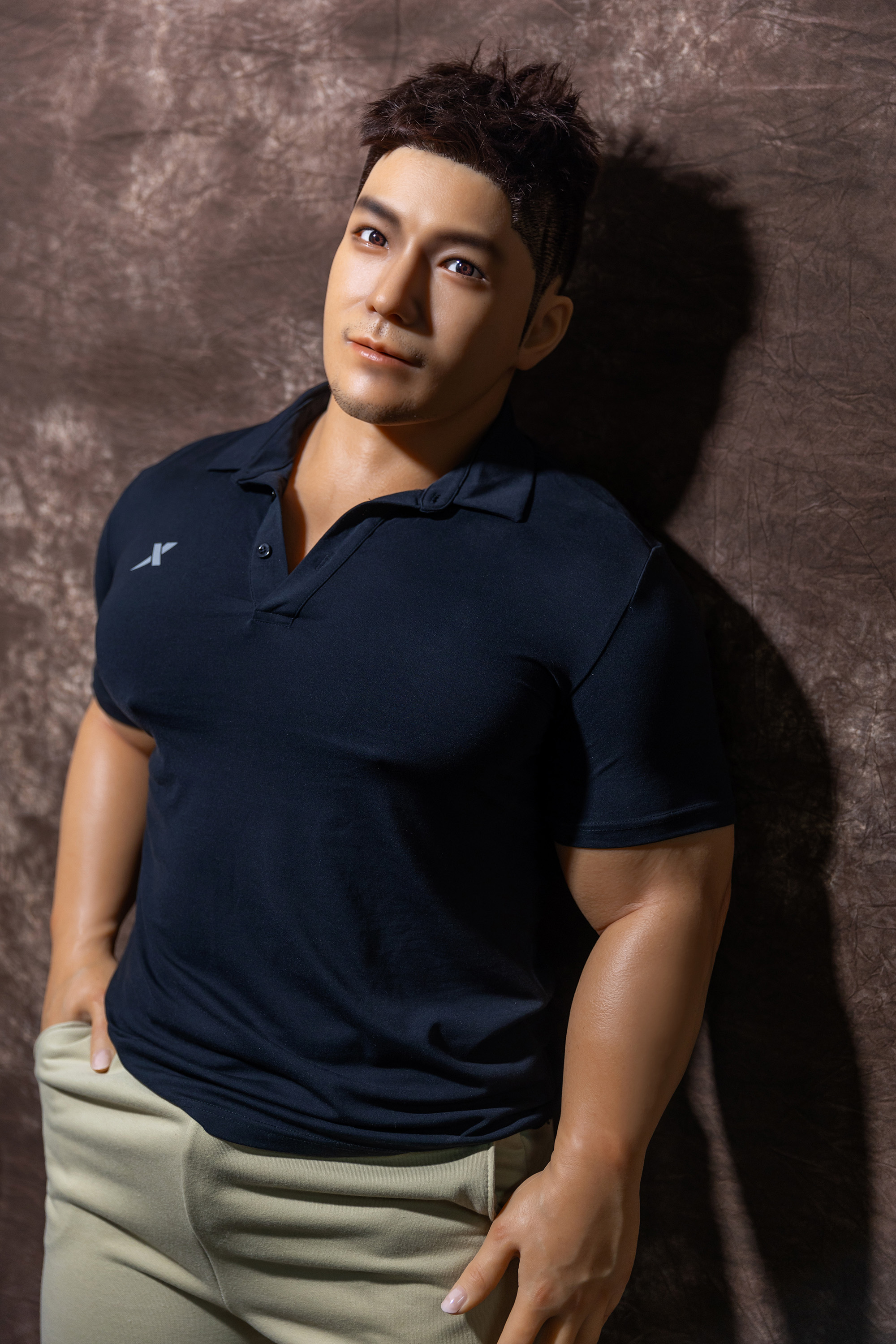 Male sex doll, wearing black polo shirt and beige pants.