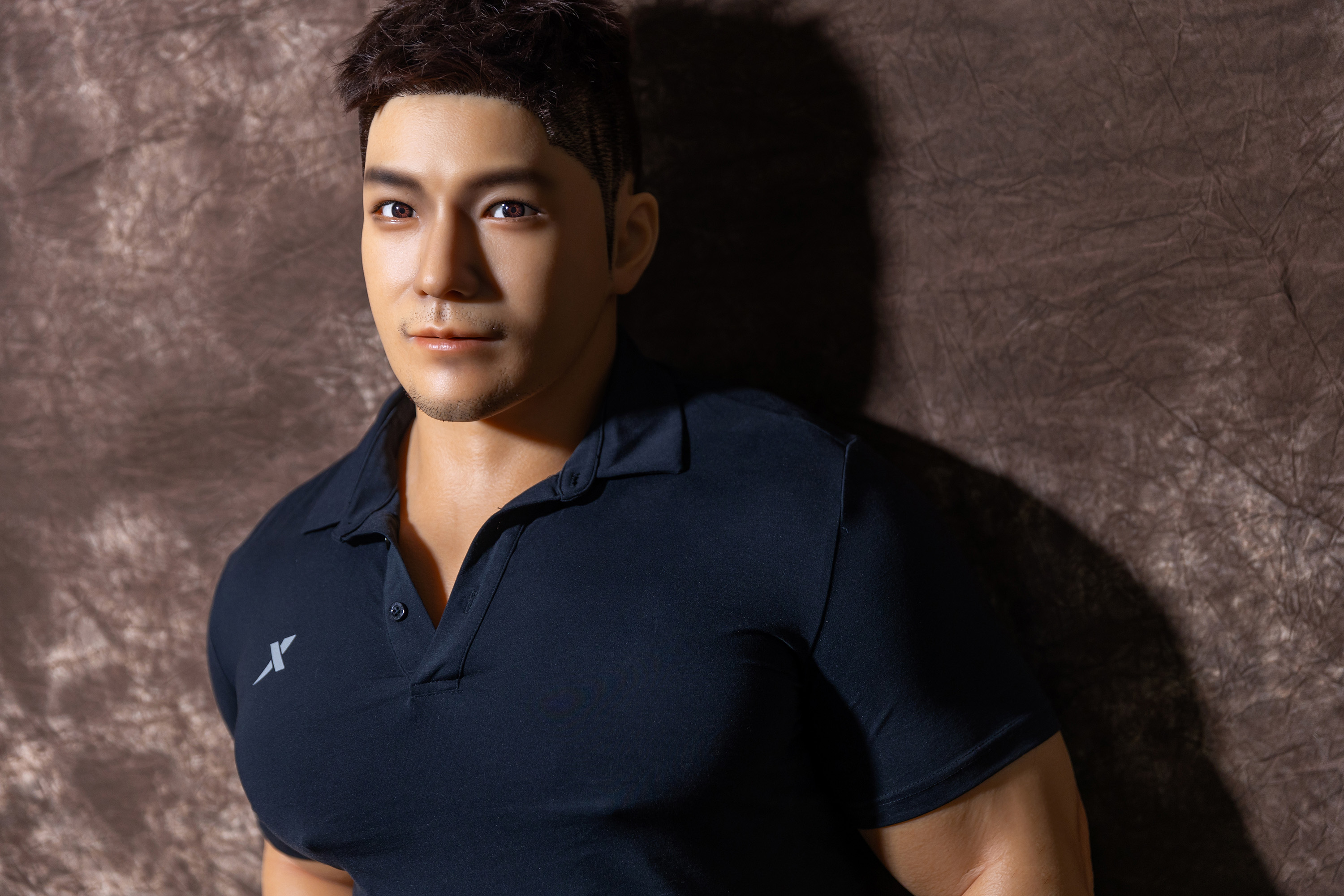 Male sex doll wearing a black polo shirt, muscular physique.